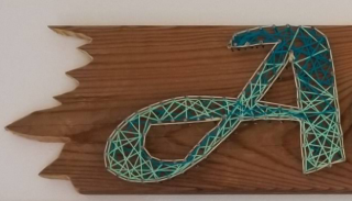 wood plank with nail-and-string art spelling out Adventure